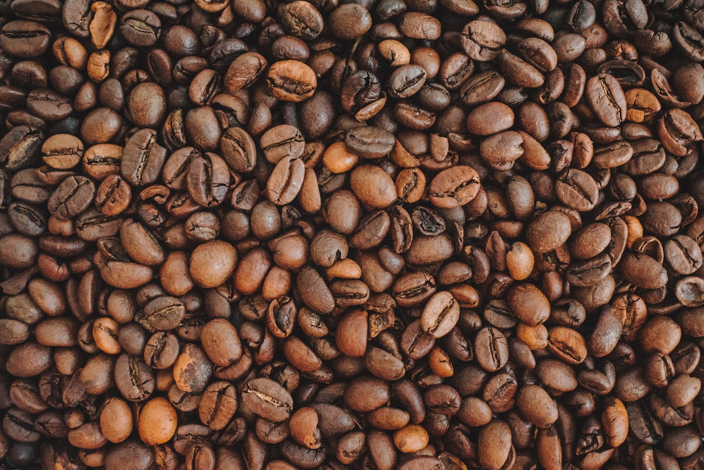 Dense, full-frame background of unevenly roasted coffee beans showing varying shades of brown